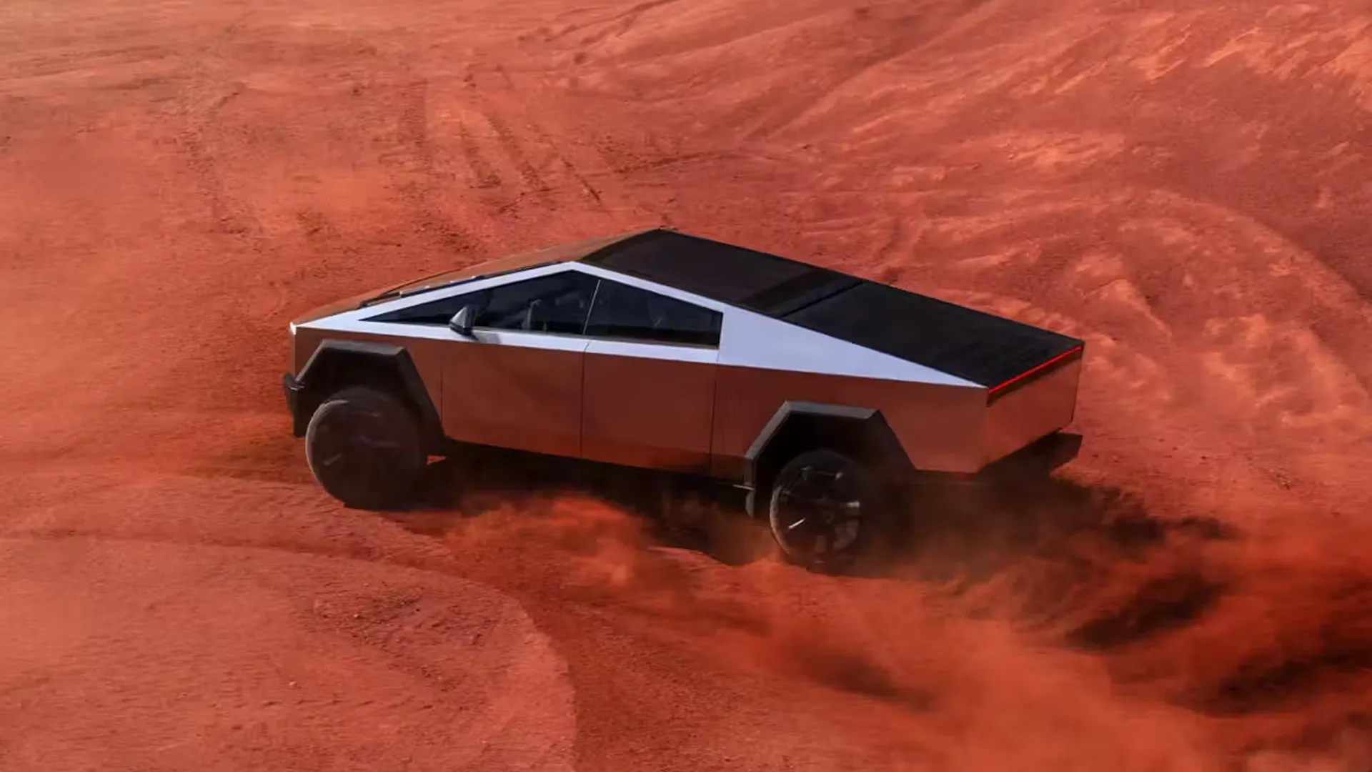A sharp-angled stainless-steel pickup truck speeding across deep red desert sand, kicking up dust, an emblem of polarizing, convention-breaking product design