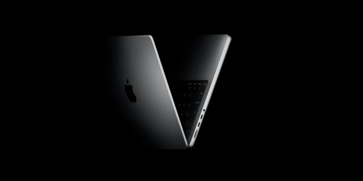 A MacBook Pro in space gray, lid half open and lit from within, forming a V shape against a black background with the Apple logo glowing on the case